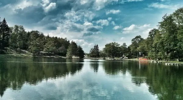 Un lago tranquillo circondato da alberi verdi, con nuvole drammatiche nel cielo. Un'oasi di pace tra i laghi dell'Emilia Romagna.
