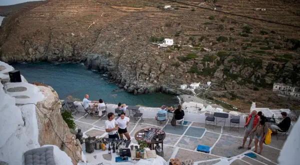 Människor njuter av en måltid på en terrass med utsikt över en vik på Sifnos, Grekland.