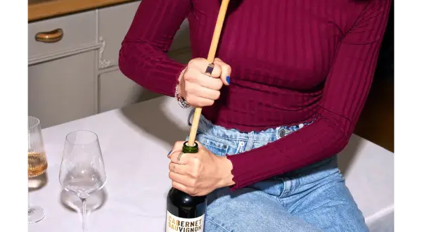 Korken ohne Korkenzieher: Eine Person versucht, eine Weinflasche mit einem Holzlöffel zu öffnen.