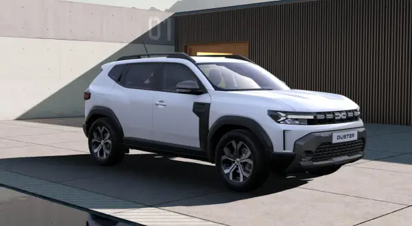 Nowa Dacia Duster w białym kolorze prezentuje się nowocześnie na tle betonowej ściany i budynku z drewnianymi elementami.