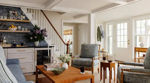 A living room with a traditional style, featuring blue patterned armchairs, a rattan coffee table, and a bar area with blue tiled backsplash.