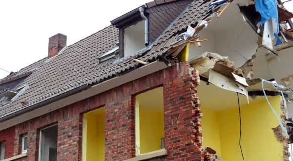 Zniszczony budynek z cegły, dach w trakcie rozbiórki. Jeśli planujesz wyburzenie budynku, sprawdź, gdzie zgłosić wyburzenie budynku.
