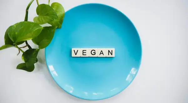 Niebieski talerz z literami "VEGAN" i zielonymi liśćmi. To symbol tego, co to jest weganizm – dieta bez produktów odzwierzęcych.