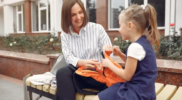 Mama i córka siedzą na ławce, przygotowując plecak. To inspiracja dla rodziców dorosłych dzieci, jak wspierać ich samodzielność.