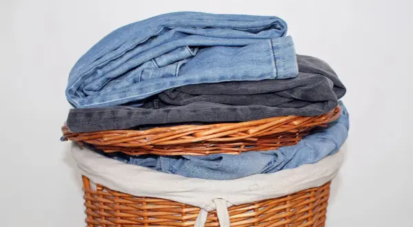 Ein Wäschekorb voller Jeans. Die oberste Jeans stinkt nach Chemie, ein deutliches Zeichen für eine neue Wäsche.