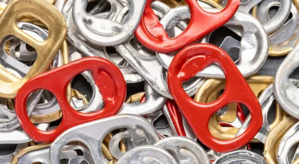Mnóstwo srebrnych, złotych i czerwonych zawleczek od puszek tworzy barwną mozaikę. Co oznaczają zawleczki od puszek? To symbol recyklingu i możliwości tworzenia z nich czegoś nowego.