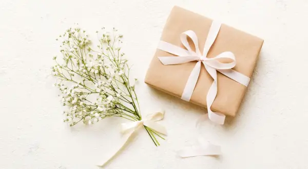 Bukiet gipsówki z kremową wstążką i prezent w papierze kraft, ozdobiony jasnoróżową wstążką. Czy kwiaty daje się w papierze? Tak, w takim eleganckim opakowaniu.