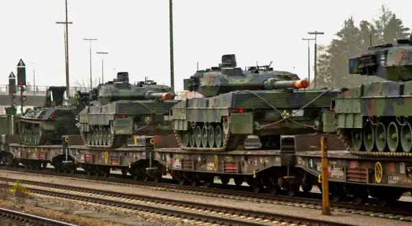 Pociąg wojskowy transportuje kilka czołgów Leopard 2 na wagonach platformach.