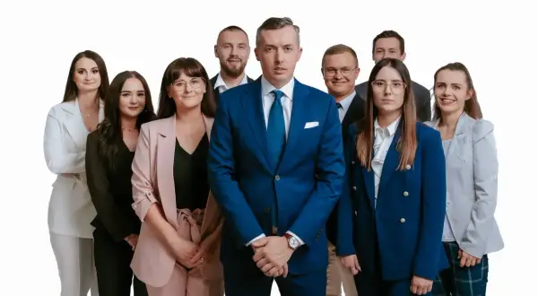 Grupa profesjonalistów w garniturach i kostiumach, stojąca przed białym tłem.