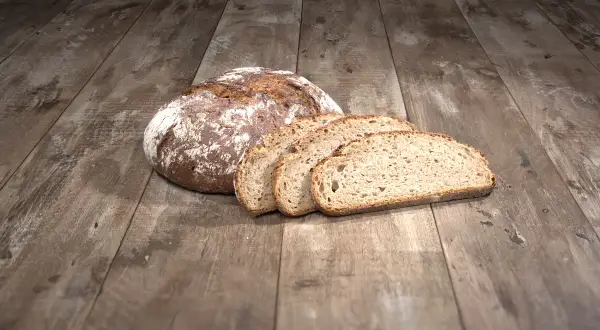 Ein Laib Brot liegt auf einem Holztisch, daneben vier Scheiben. Die ideale Kerntemperatur Brot ist erreicht.