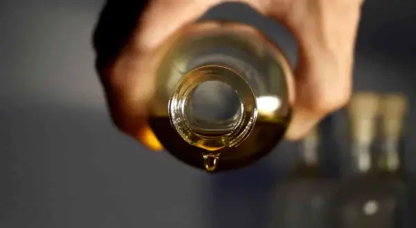 Une goutte d'huile dorée tombe d'une bouteille, parfait pour votre huile cheveux maison.