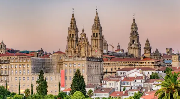 Majestatyczna katedra w Santiago de Compostela góruje nad miastem. W tle widać budynki i palmy.