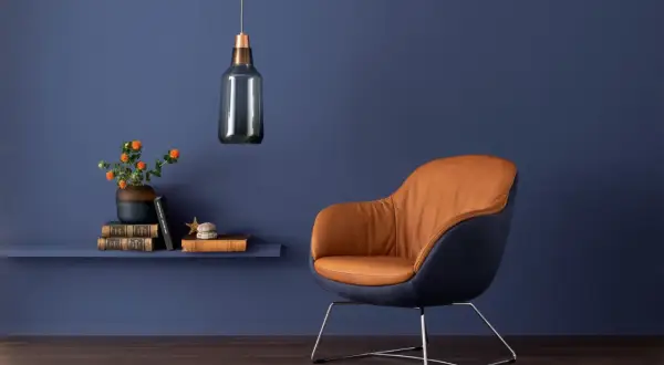 Ein Sessel mit cognacfarbenem Leder und dunkelblauem Stoff vor einer tiefblauen Wand. Die blau wandfarbe wirkung schafft eine ruhige Atmosphäre.