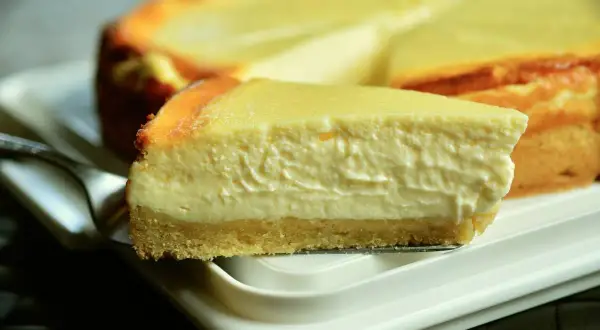 Pyszny sernik na białym talerzu, idealny do lodówki. Gdzie przechowywać sernik po upieczeniu? W chłodnym miejscu!
