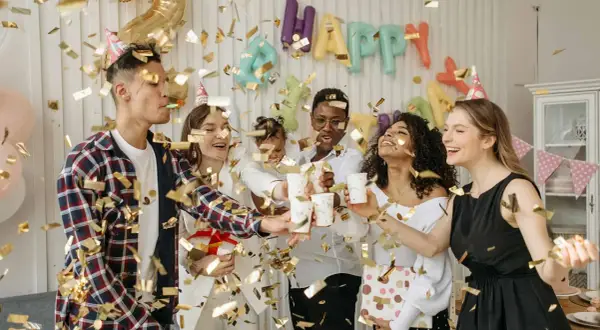 Fröhliche Freunde feiern eine Geburtstagsparty mit Konfetti und Luftballons. Ein "Happy Birthday"-Banner hängt im Hintergrund. Ein tolles Lied für Erwachsene!