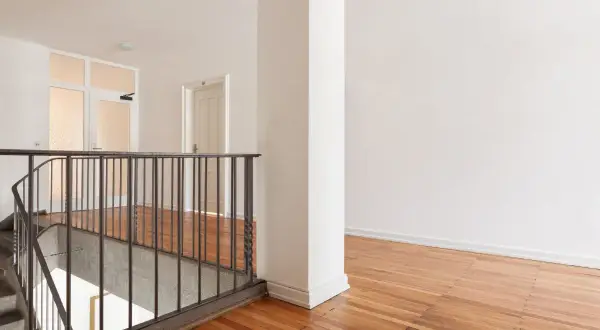 Jak pomalować wysoką klatkę schodową? Jasne wnętrze z drewnianą podłogą i metalową balustradą.