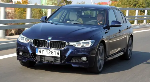Ciemnoniebieskie BMW F30 M Pakiet pędzi po drodze. Kierowca skupiony na trasie.