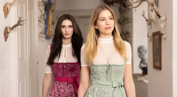 Zwei Frauen in Tracht, eine mit dunkelbraunem, die andere mit blondem Haar, präsentieren elegante dirndlschürzen lang.