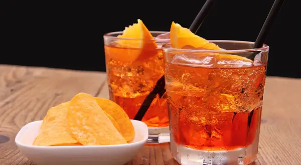 Dwa orzeźwiające drinki z pomarańczą i słomkami, obok miseczka chipsów. Idealne aperitif przykłady na letnie popołudnie.