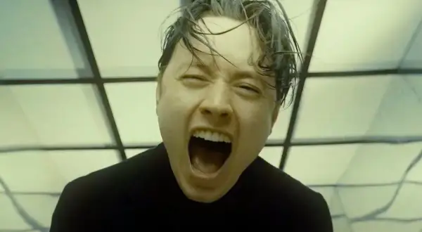 Noah Sebastian screams in a black shirt, his hair wet and messy, against a backdrop of geometric patterns.