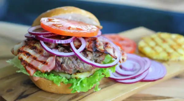 Burger z bekonem, sałatą, pomidorem i czerwoną cebulą na desce.