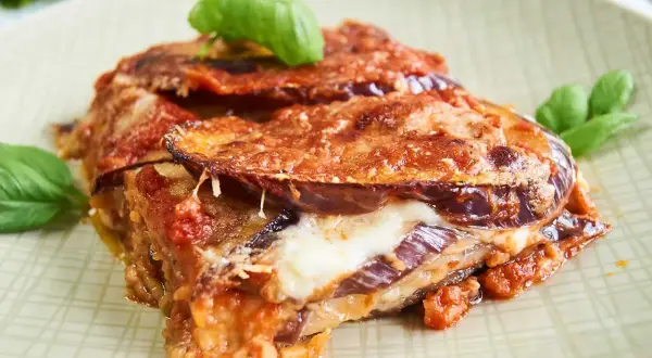 Parmigiana di Melanzane auf einem Teller mit Basilikum garniert.