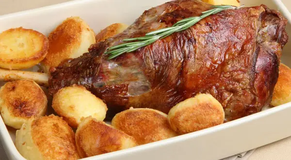 Succulento agnello al forno con patate arrosto dorate, guarnito con rosmarino fresco.