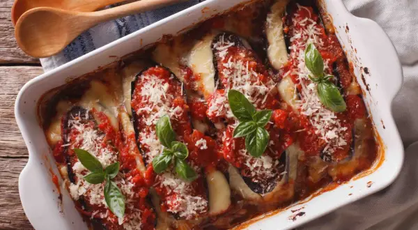 Un plat d'aubergine à la parmesane gratinée, garni de sauce tomate, fromage fondant et basilic frais.