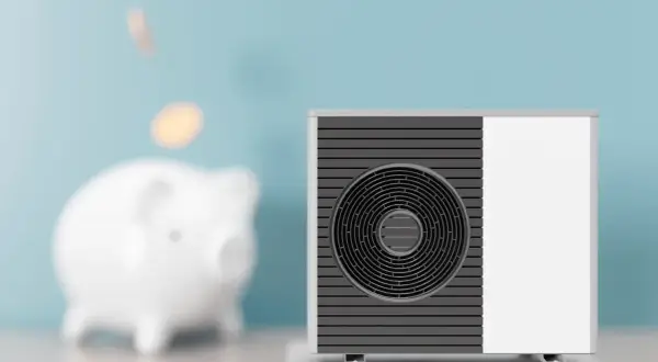 Scaldacqua a pompa di calore: svantaggi e risparmio. Un salvadanaio a forma di maialino con monete che cadono, accanto a un'unità esterna.