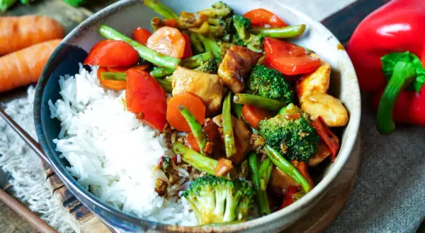 Schüssel mit Reis und buntem Chop Suey: Hühnchen, Brokkoli, Karotten, Paprika und grüne Bohnen in einer herzhaften Sauce.