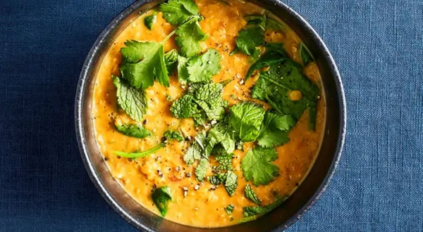 Ein dampfender Linsen-Curry in einer Schüssel, garniert mit frischem Koriander und Minze.