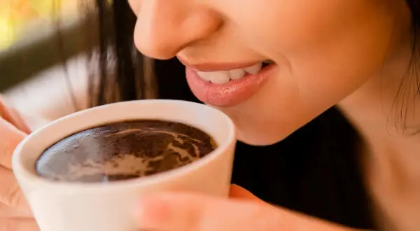 Uśmiechnięta kobieta delektuje się aromatyczną kawą po wszczepieniu implantu.