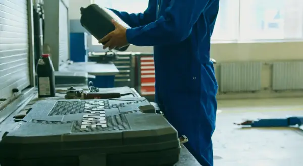 Meccanico in tuta blu prepara il cambio olio motore fuoribordo 4 tempi, tenendo una tanica di olio.