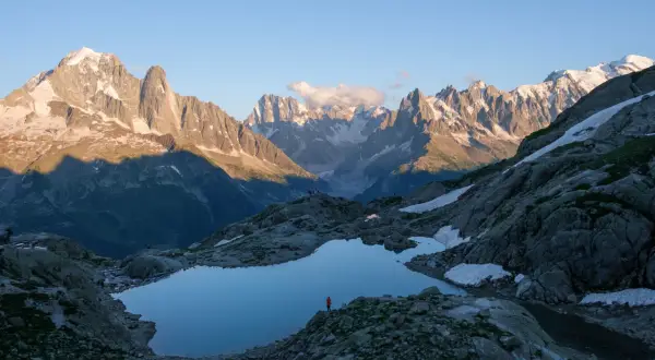 Un randonneur solitaire admire le reflet des Aiguilles Rouges dans un lac d'altitude. Le soleil couchant éclaire les sommets enneigés.