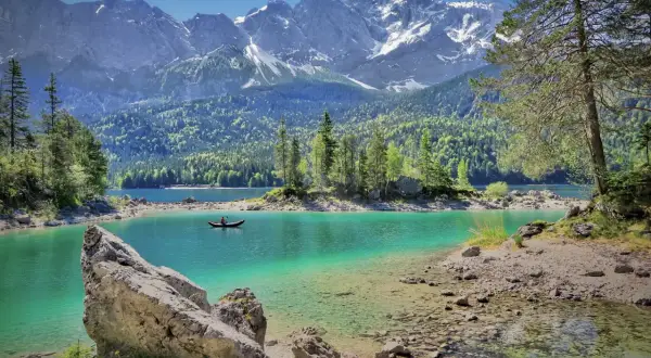 Türkisblaue Bergseen und schneebedeckte Gipfel – das sind die Attraktionen Bayerns. Ein Kajakfahrer gleitet über das klare Wasser.