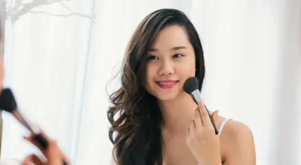 Une jeune femme applique du maquillage pour peau grasse avec un pinceau.