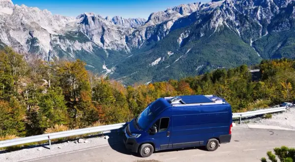 Blauer Campervan auf Bergstraße in Albanien. Perfektes Wetter im August für eine Reise durch die beeindruckende Berglandschaft.