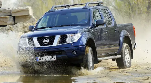 Niebieski Nissan Navara pokonuje wodną przeszkodę, rozpryskując błoto.