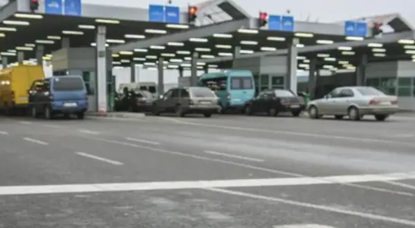 Kolejka samochodów na granicy polsko rosyjskiej. Widać budynki przejścia granicznego, sygnalizację świetlną i różne pojazdy.
