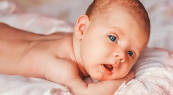 Niemowlę z niebieskimi oczami leży na brzuchu. Delikatny meszek, czyli lanugo, pokrywa jego plecy.