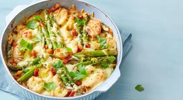 Herzhafter Spargel Auflauf mit Kartoffeln, Speck und geschmolzenem Käse, garniert mit Petersilie und Zitronenschale.