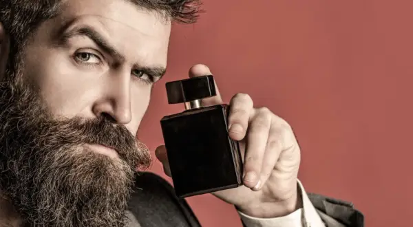 Mężczyzna z brodą trzyma czarną buteleczkę perfum, zastanawiając się, gdzie psikać perfumy, by podkreślić swój styl.
