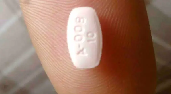 Biała tabletka z oznaczeniem "A-009 10" na palcu. Może to być lek, np. Abilify, pomagający w leczeniu schizofrenii.