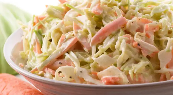 Miseczka surówki coleslaw z poszatkowanej kapusty i marchewki w kremowym sosie.