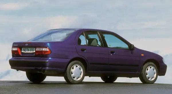 Fioletowy Nissan Almera z lat 90. stoi na tle błękitnego nieba.