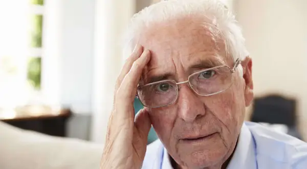 Älterer Mann mit Brille, der sich an die Stirn fasst, wirkt nachdenklich, vielleicht wegen Morbus Korsakow.
