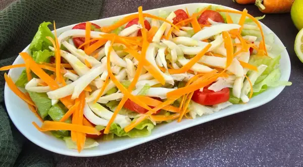 Deliziosa insalata di seppie con lattuga croccante, carote julienne e pomodorini freschi. Un piatto leggero e saporito.