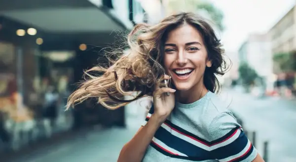 Lachende Frau telefoniert, ihr Haar weht im Wind. Sie genießt ihr **iu auslandssemester** in der Stadt.