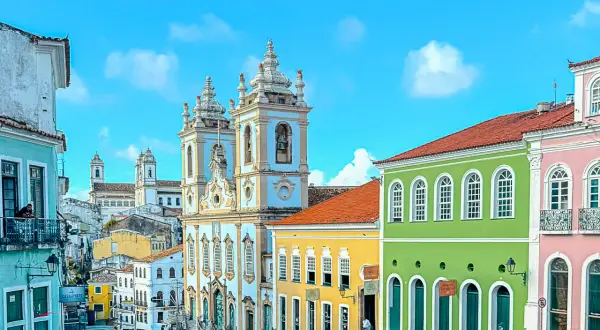 Calles empedradas y coloridas casas coloniales bajo un cielo azul en **Bahía, Brasil**. Una iglesia barroca domina el paisaje.