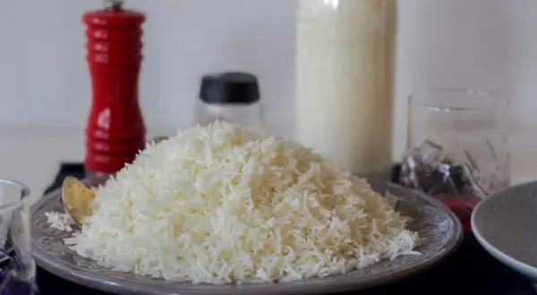 En stor hög med fluffigt, nykokt basmatiris på en tallrik. Bredvid står en röd pepparkvarn och en flaska mjölk.